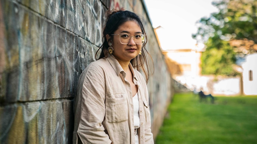 Rosario in a park, leaning against wall with graffiti on it.