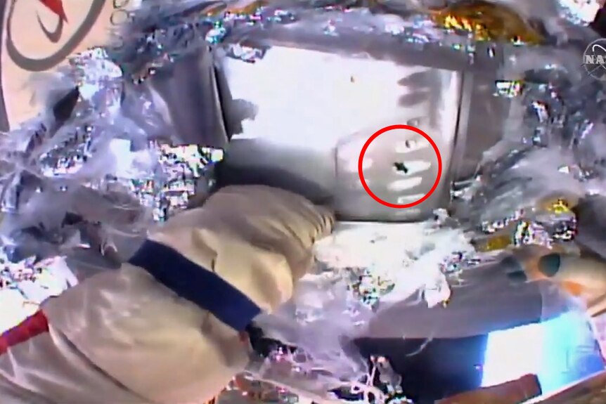 A small hole in metal plating is visible after the heat shield is peeled back.