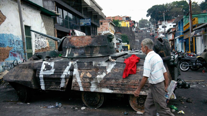 Man walks by car tank during Venezuela protests