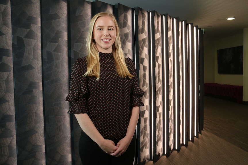 Dr Melanie Neeland stands in front of a feature wall.