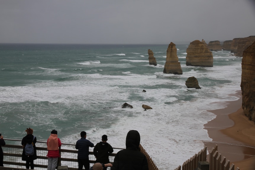 Tourists stand in gloomy weather staring out to sea at the 12 Apostles.