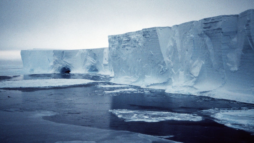 An iceberg in Antarctica, with deep blue water in the foreground.