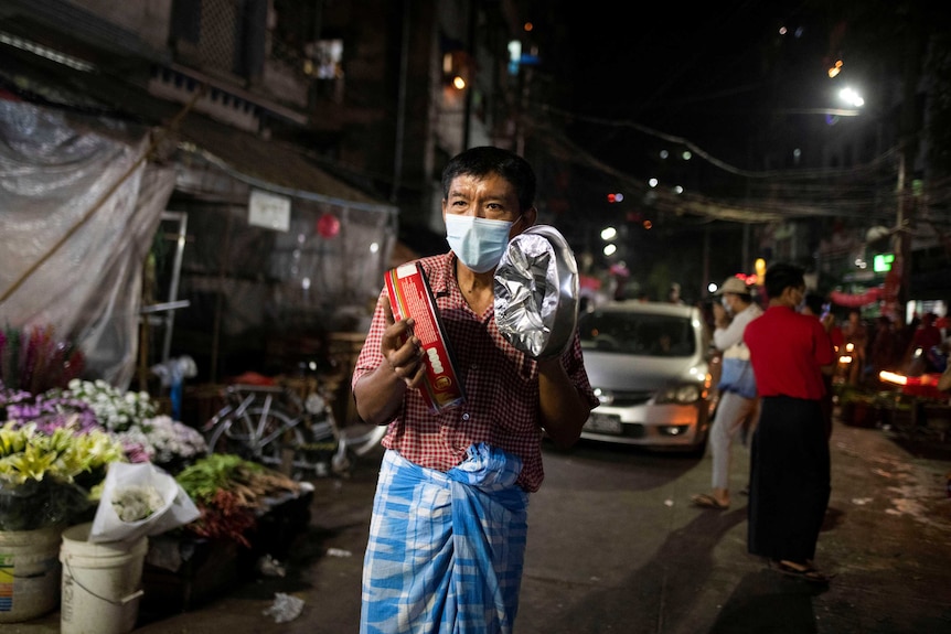 A man in a face mask bangs pots at night wearing a face mask.