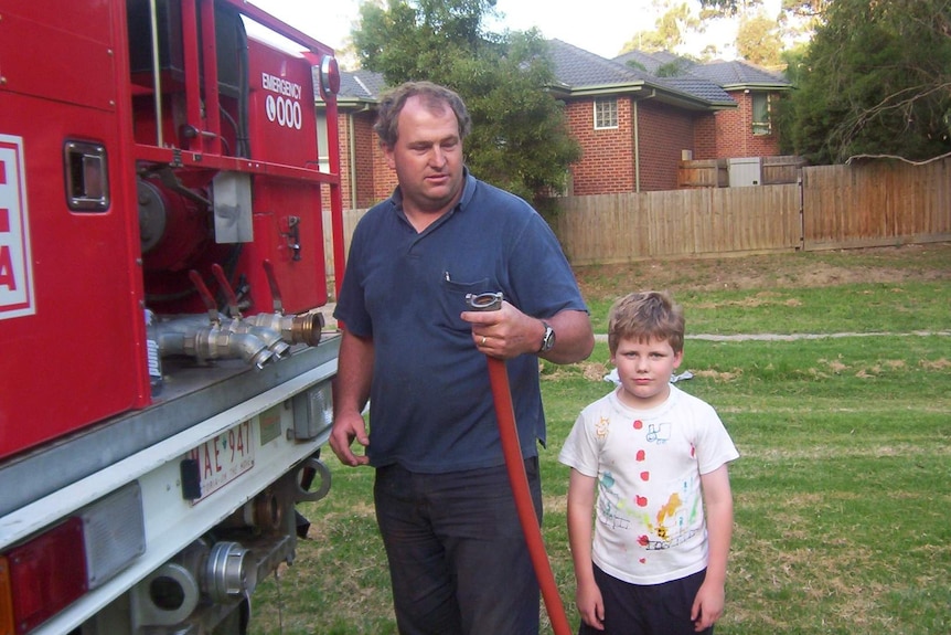 A man and a boy stand next to a red truck