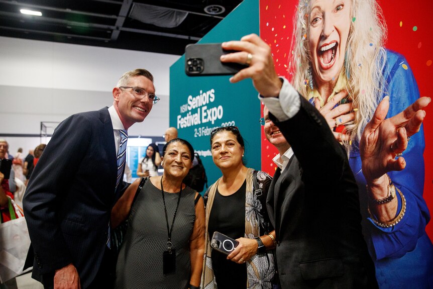 a man wearing glasses smiling and getting a selfie with two women