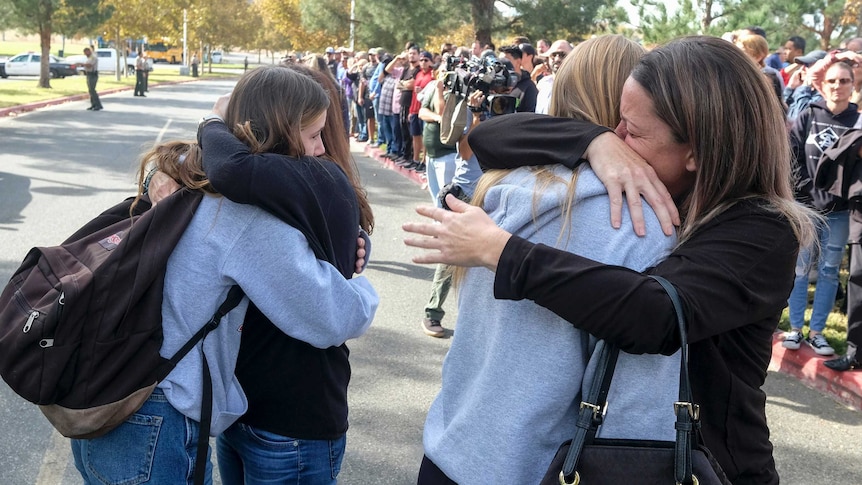 Tearful students hug their parents in a park.