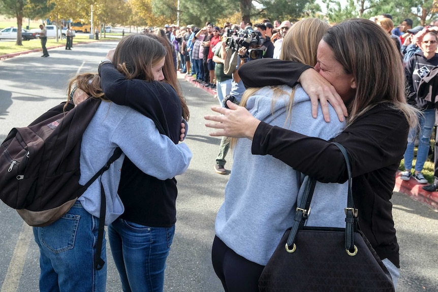 Tearful students hug their parents in a park.