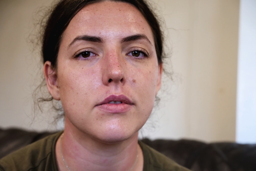 a woman with brown hair looks into the camera, a serious expression on her face