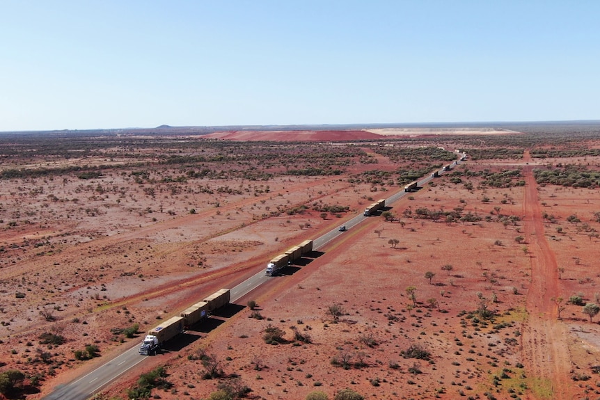 Aerial shot of truck convoy driving through dry, red country