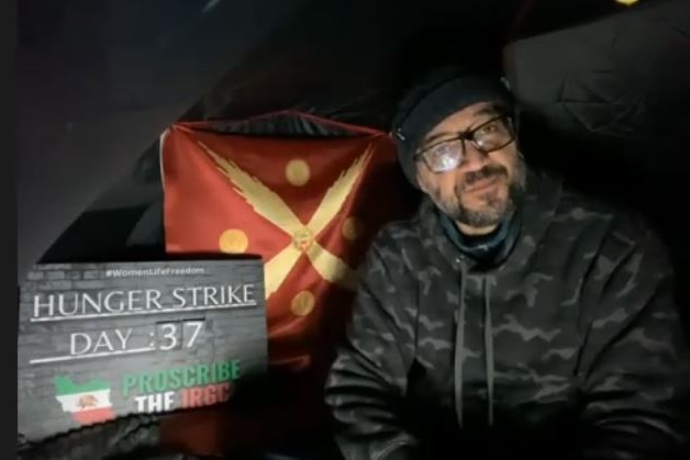 Man in a dark tent with protest sign about a hunger strike next to him.