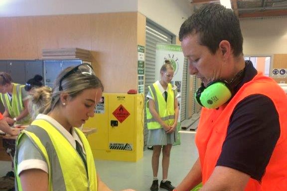 Simon Curry teaches a female high school student at a carpentry course