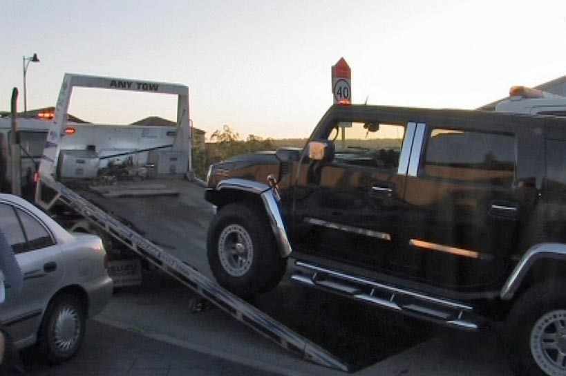 A large black SUV is hauled onto the back of a flatbed truck.