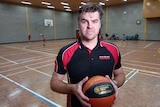 Grant looks serious, holding a basketball on a court.