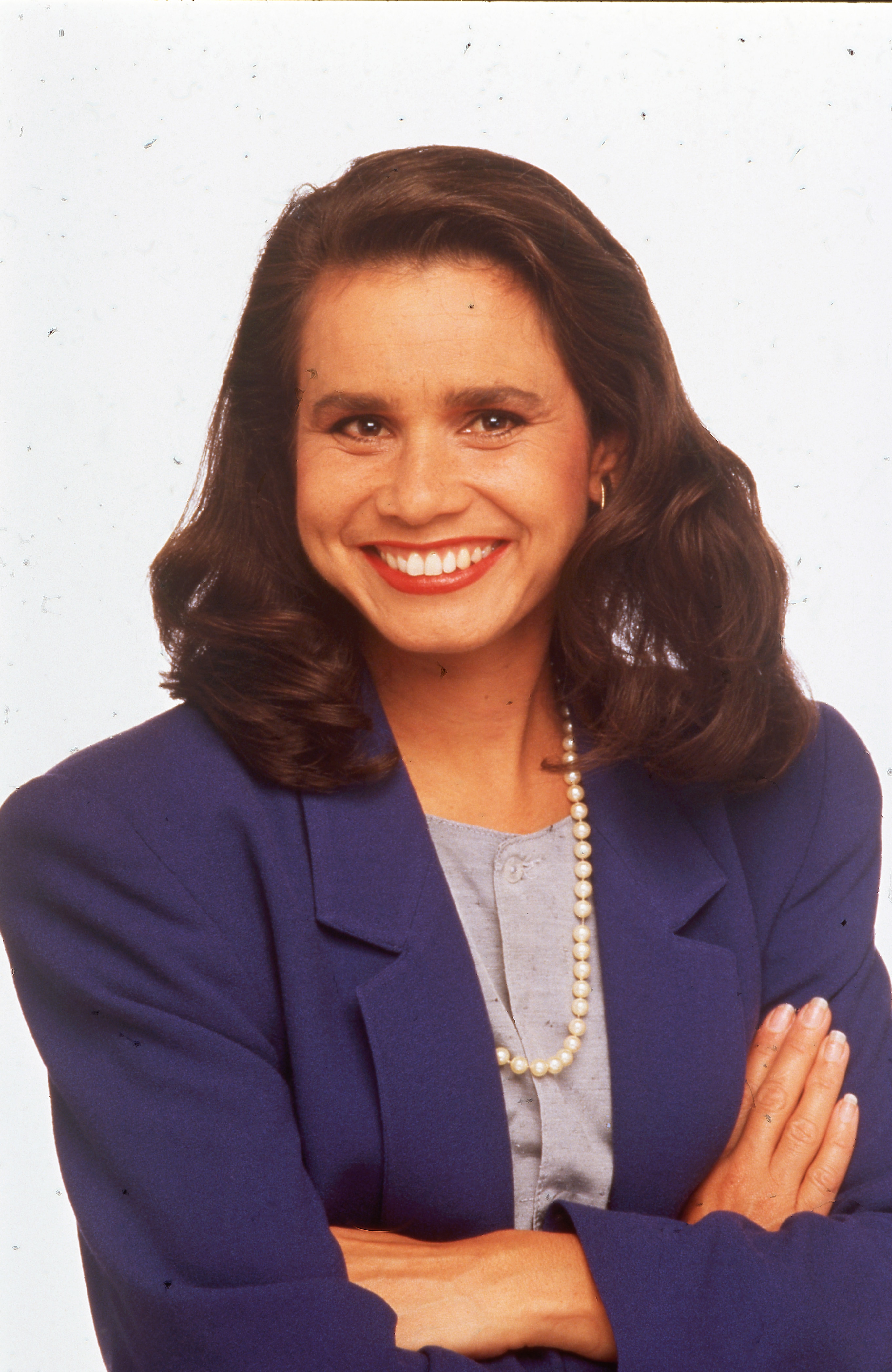 A young rhoda in a suit with her arms crossed. She smiles at the camera