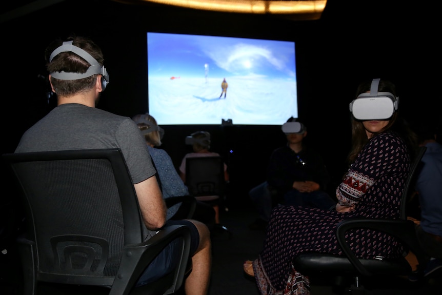 Two people sit in the dark with virtual reality headsets