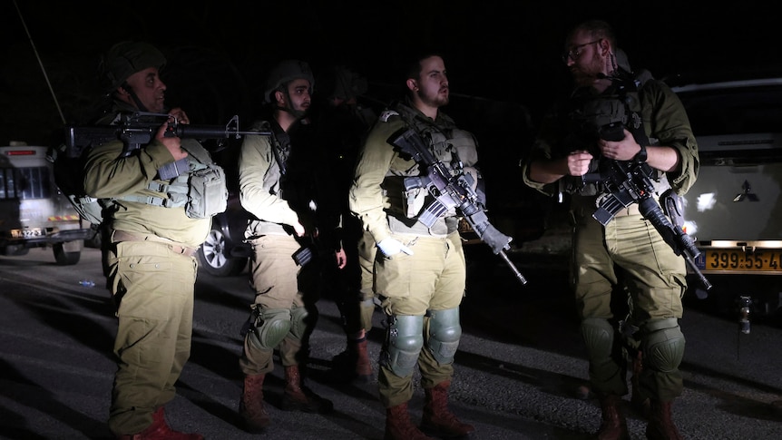 Israeli soldiers lit up by car head lights during an evening patrol.