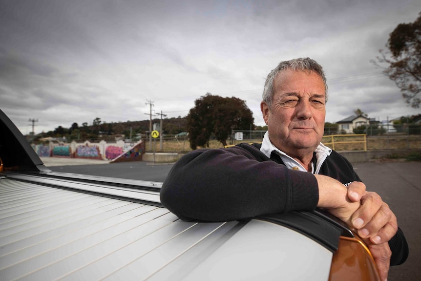 A middle aged man leans against a white ute