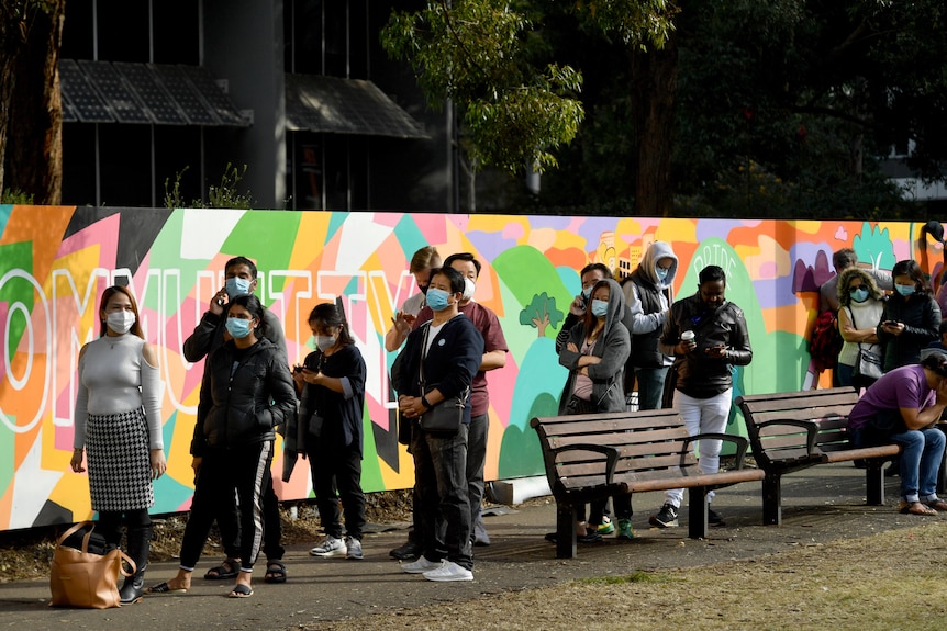 a line of people wearing masks standing next to a brightly coloured wall