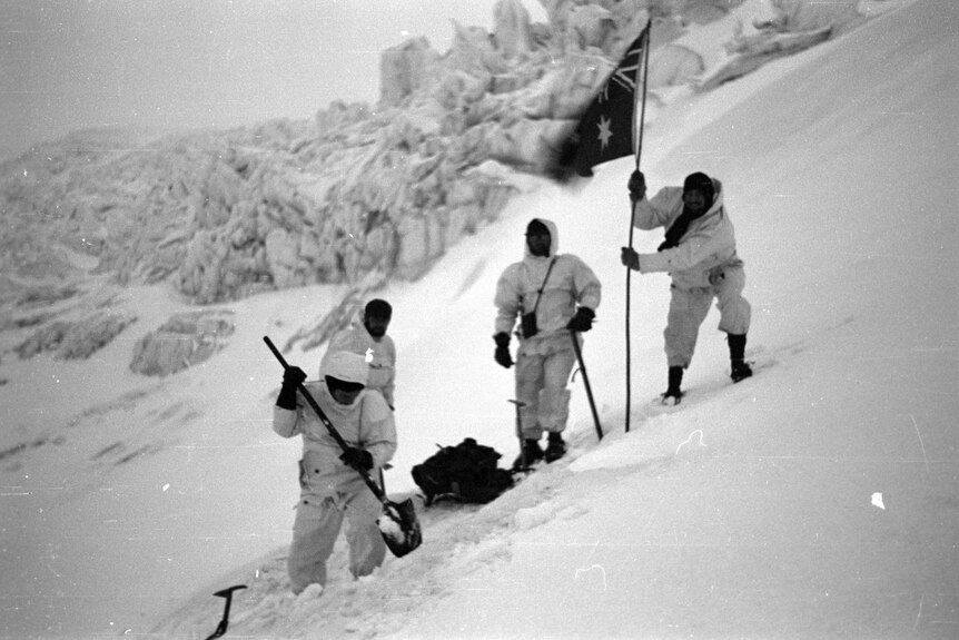 Expeditioners plant an Australian flag while attempting to climb Big Ben. The photo was taken in 1953