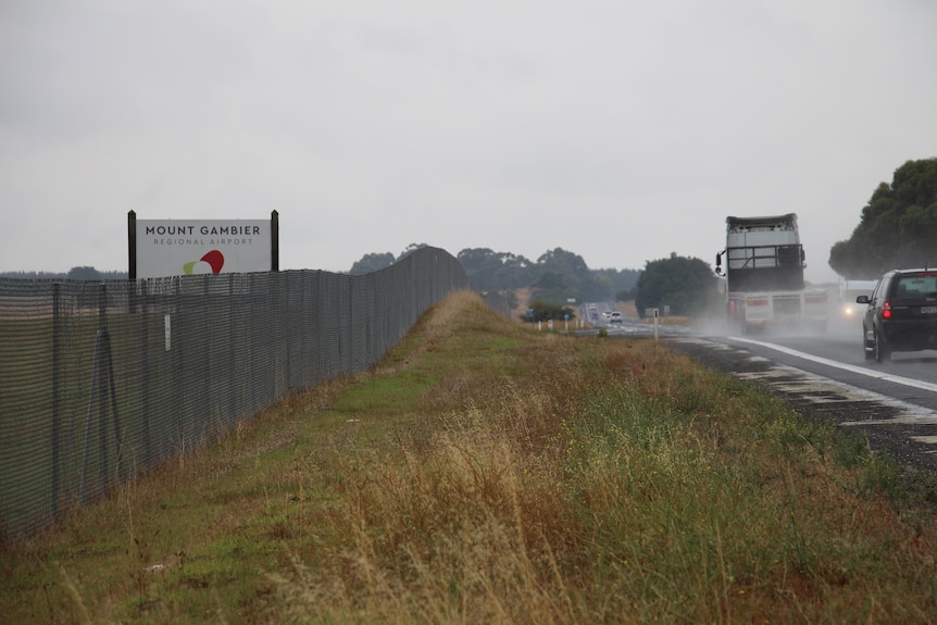 A fence line along the left with a grass strip and a highway on the right