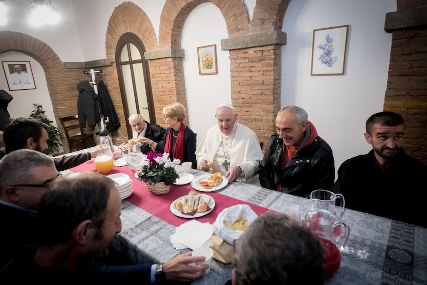 Pope Francis sharing a meal in a building with some people at a table