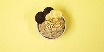 Banana nice cream in a bowl topped with chocolate cookies, peanuts and banana slices.