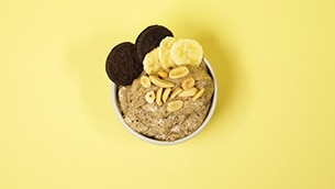Banana nice cream in a bowl topped with chocolate cookies, peanuts and banana slices.