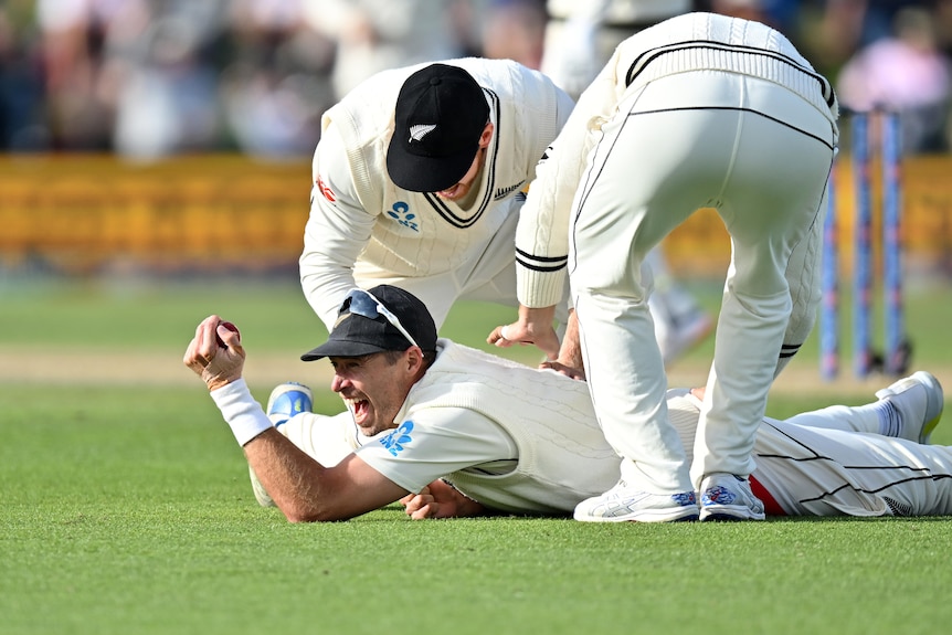 Tim Southee smiles on the ground holding onto a ball with two men hitting his back