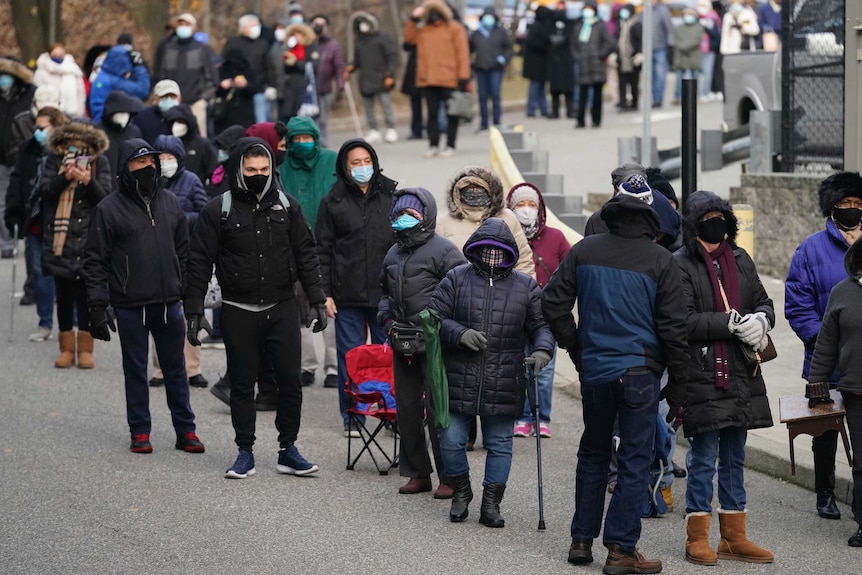 A long line of people on the street. All are wearing winter clothes and face masks.