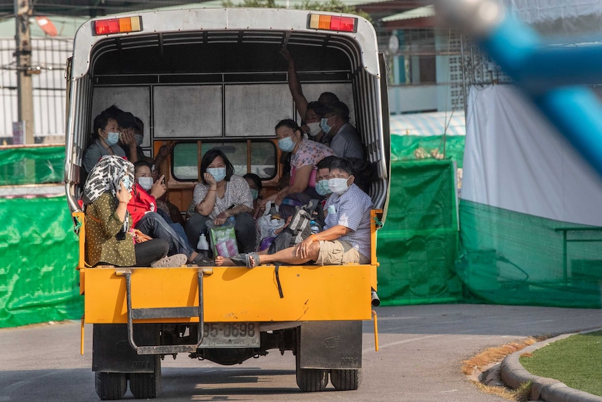 A group of migrant workers wearing masks sitting in the back of a truck.
