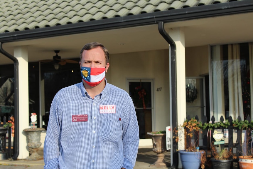 A man wearing a face mask stands in front of a house.