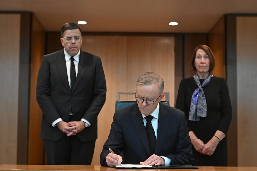 Milton Dick and Sue Lines stand behind Anthony Albanese while he signs a book inside Parliament House