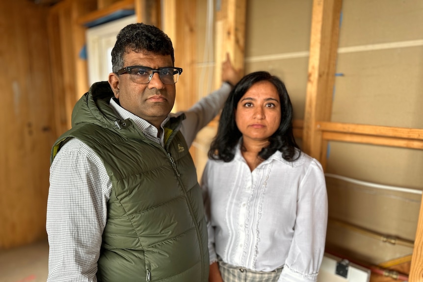 Siddarth holds the frame of a partially constructed building and Chetna stands beside him.