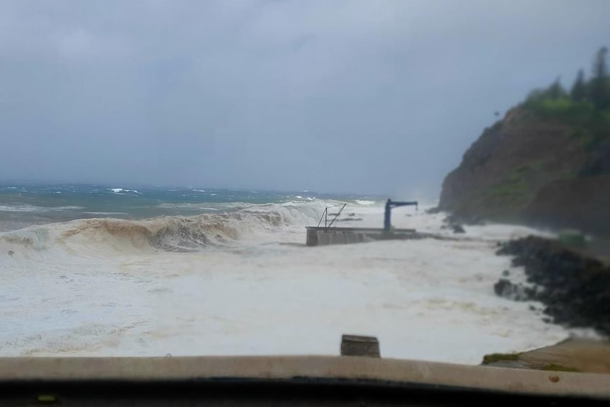 large waves crash towards cascade pier crane on norfolk island