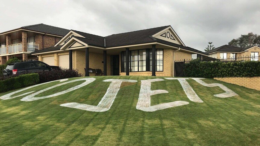 A green lawn in front of a house has the words GO JETS painted on it