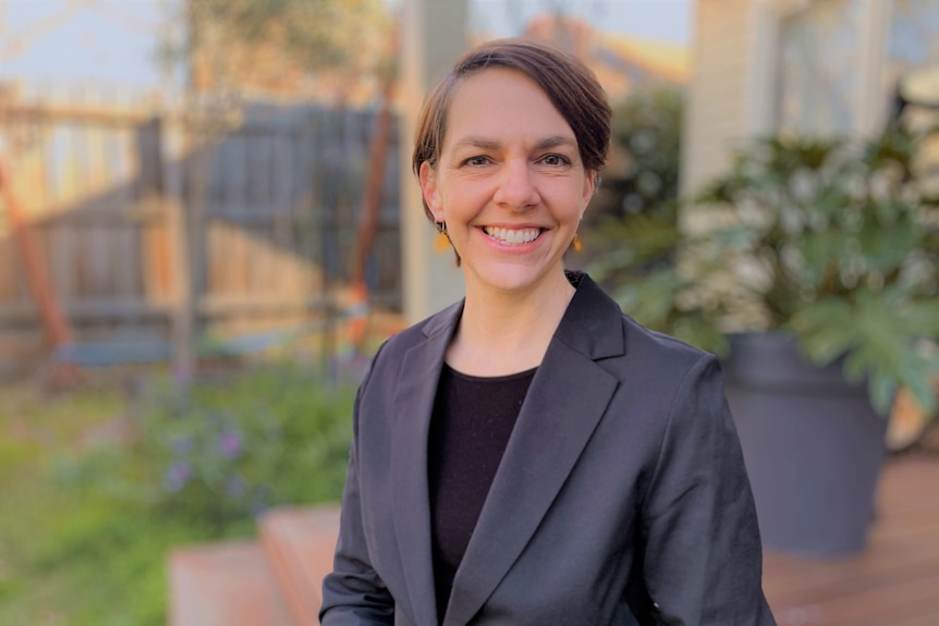 A woman smiling to camera while sitting with plants in the background