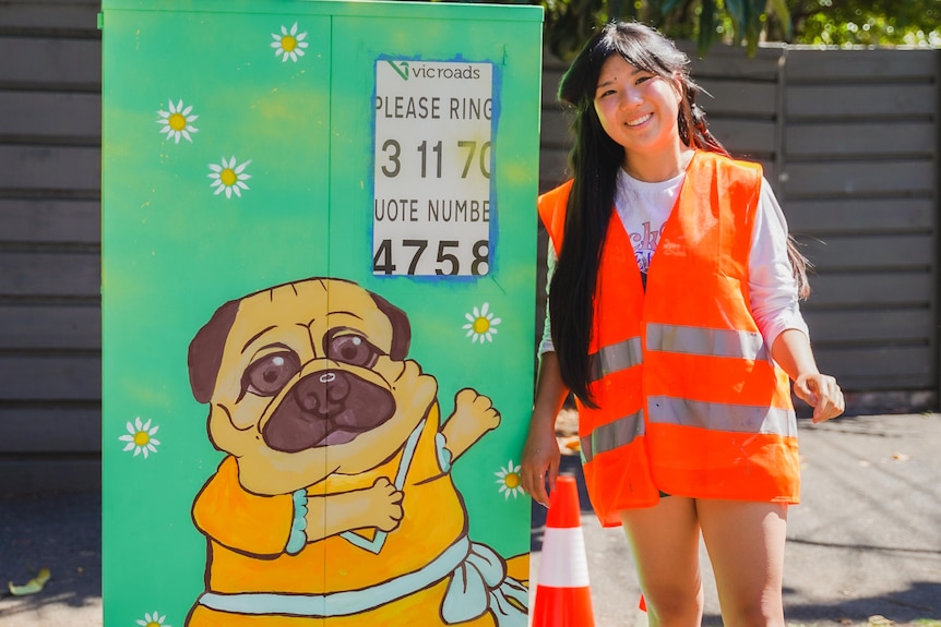 A woman standing beside a mural of a dog.