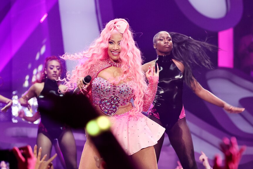 nicki minaj performs on stage wearing a bright pink bedazzled costume and long pink wig with a pink bow