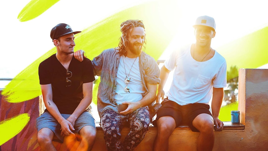 Three young men, who look like they're in their 20s, sitting on a wall and laughing.