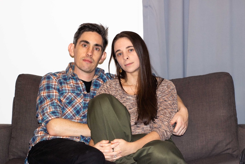 Alyse Brown and her partner Geoff sit on a couch together.