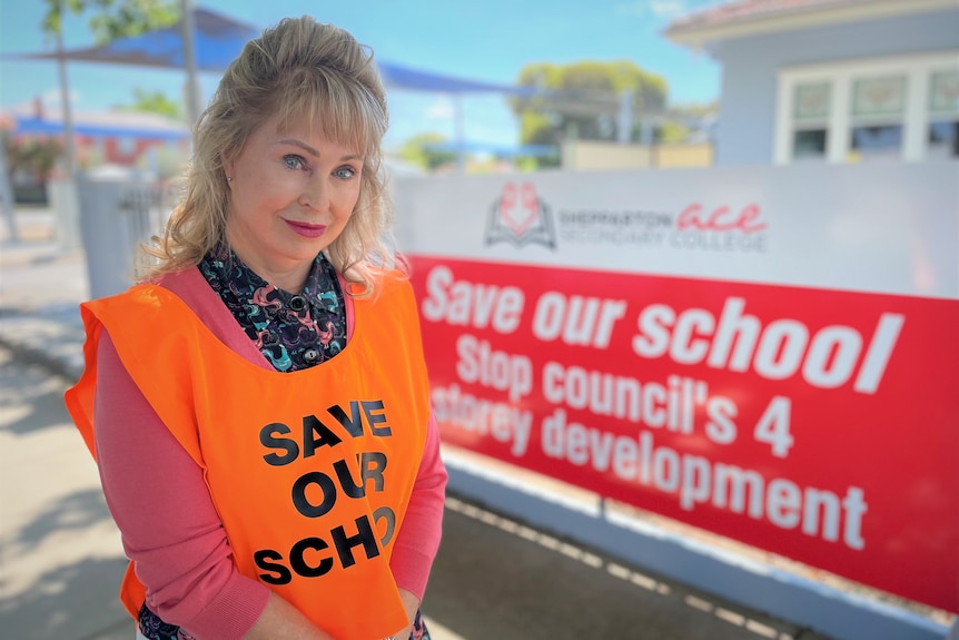 Една жена стои пред табела с надпис „Спасете нашето училище“.