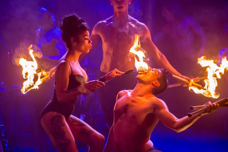 Fire-eater Heather Holliday in burlesque costume performing fire act with two male performers.
