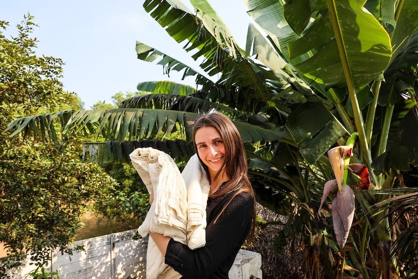 Woman stands amid lush garden as she holds material made from plant-based fibre.