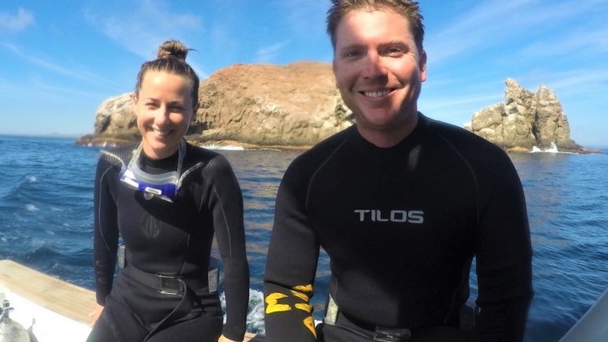 A couple aboard a boat in wetsuits.