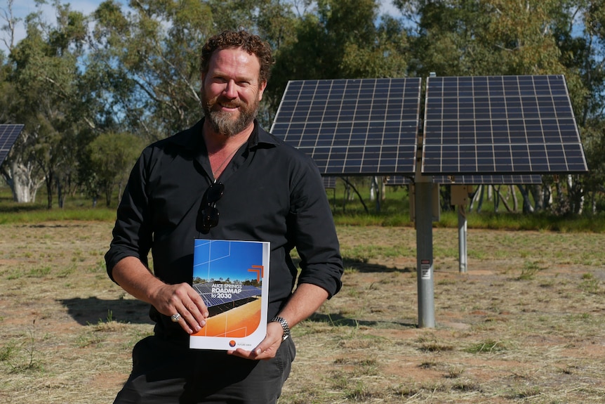 A man wearing a black shirt holds the Alice Springs roadmap to 2030 booklet in front of him.