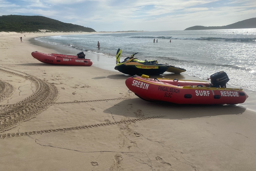 Two rubber surf life saving boats, sitting on the sand at a beach.