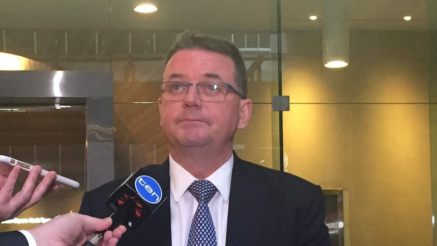 Logan City Mayor Luke Smith stands outside the Crime and Misconduct Commission in Brisbane in suit with two microphones in front