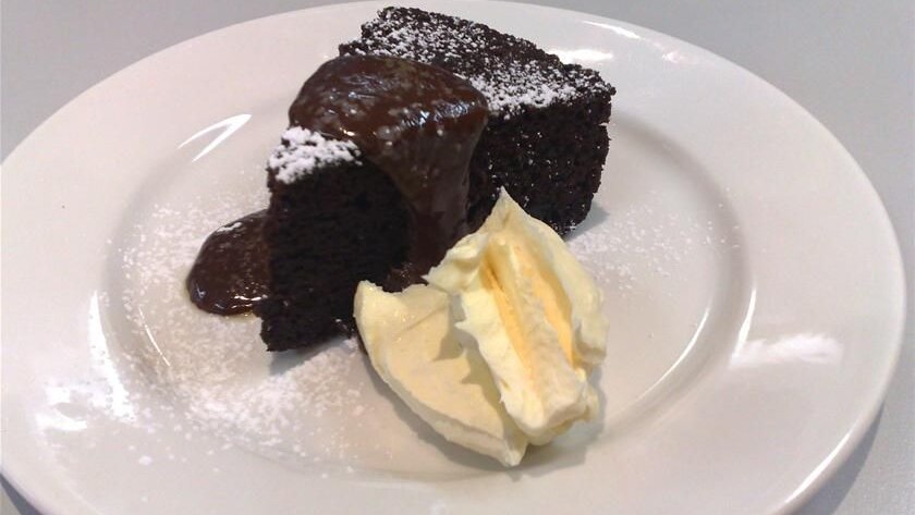 A slice of chocolate cake with mascarpone and chocolate sauce, all on a white plate.