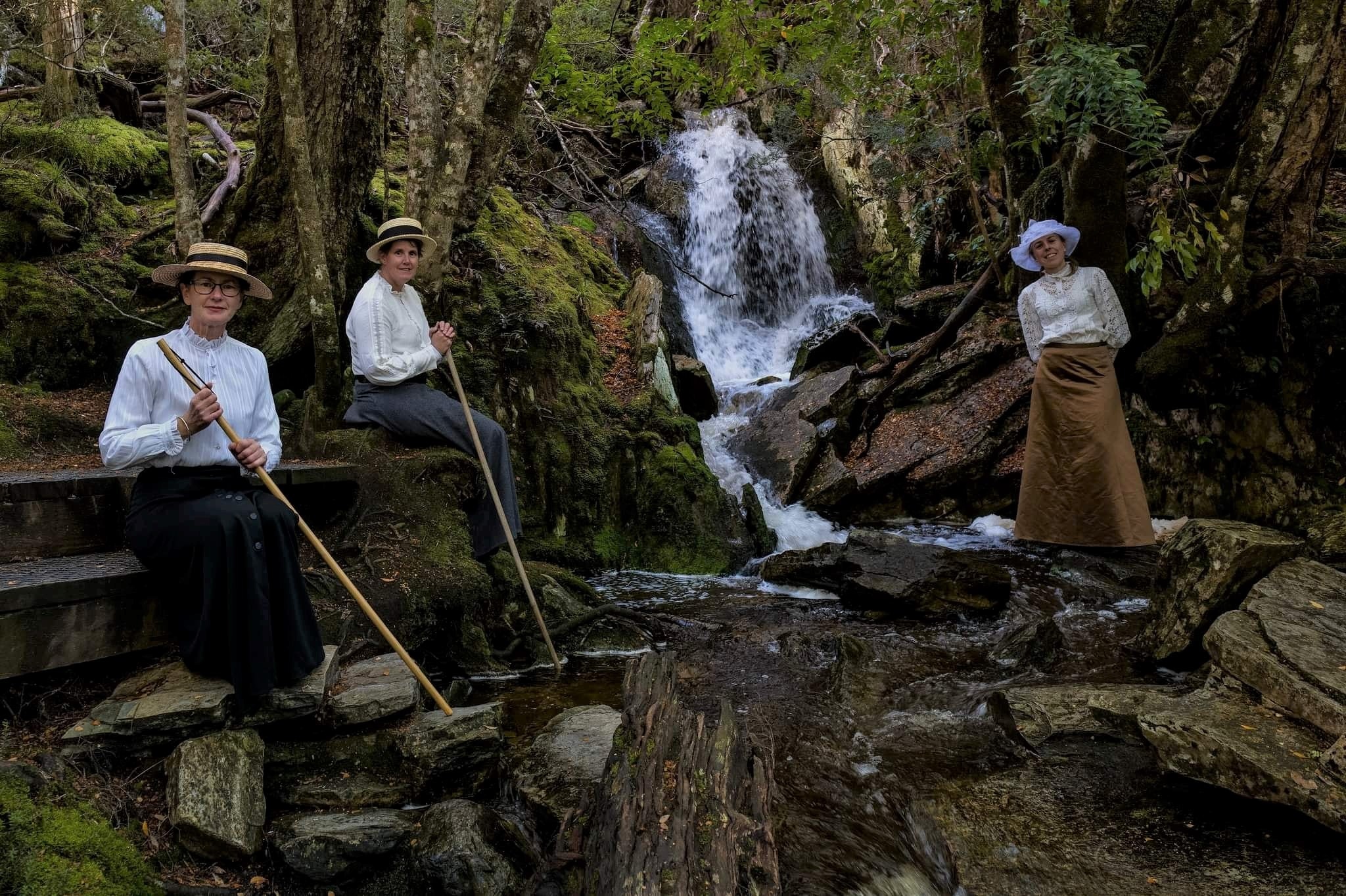 Three women in Edwardian dress posing by a waterfall.