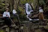 Three women in Edwardian dress posing by a waterfall.